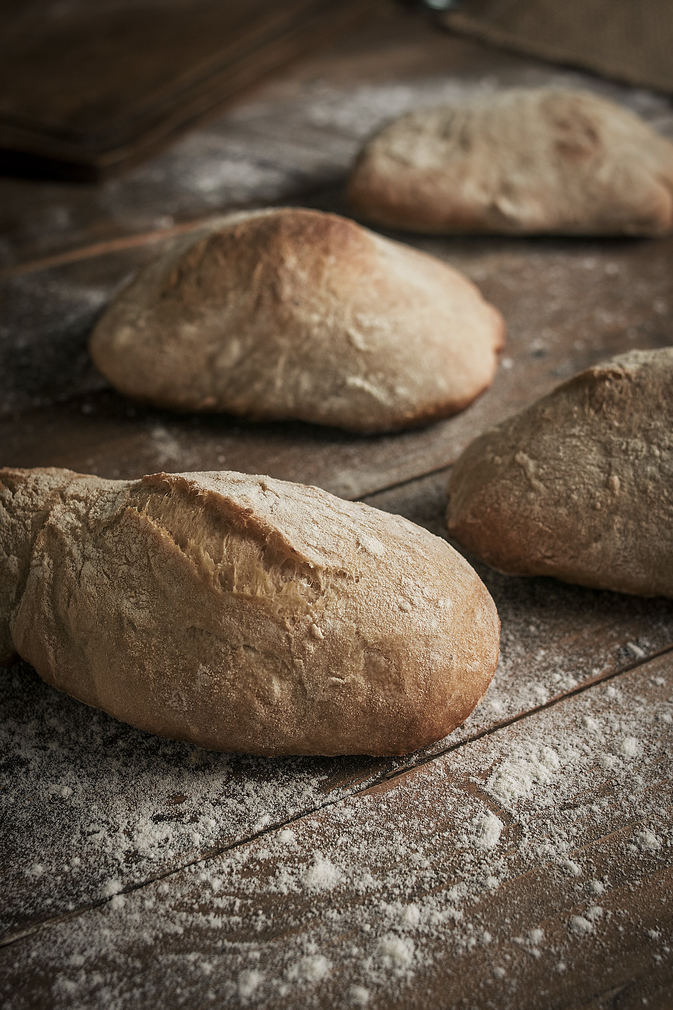 Finished no-knead ciabatta rolls on a flour-dusted wooden surface.